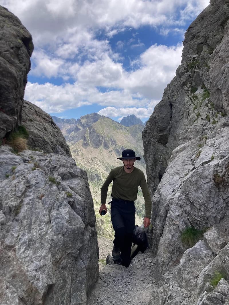 Un randonneur remonte un couloir rocheux, sac au dos, face aux sommets des Alpes